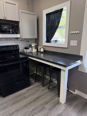 Una cocina con estufa negra, armarios blancos, una ventana con cortina negra y una zona de café.