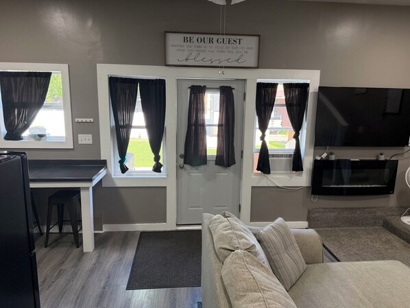 A living room with a sofa, a TV, a desk, and a door with curtains.