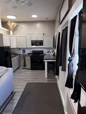 A modern kitchen with white cabinets, a black refrigerator, a microwave, and a stove.