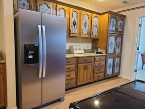 Una cocina con refrigerador de acero inoxidable, gabinetes de madera con puertas de vidrio y encimera de granito.