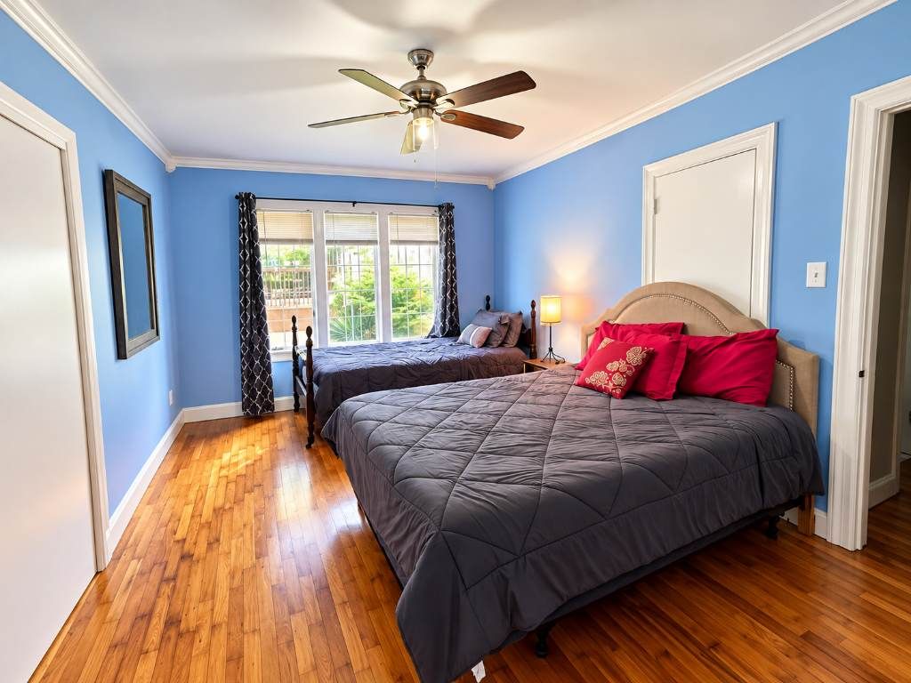 Un dormitorio con dos camas, ventilador de techo, ventana con cortinas y una puerta.