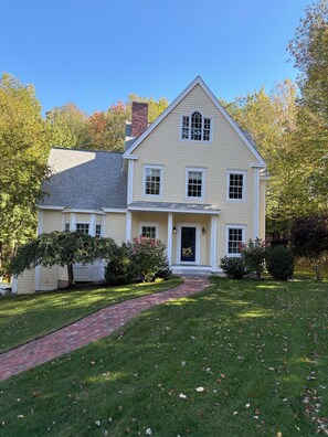 A two-story house with a front porch, a brick pathway leading to the entrance, and a well-maintained lawn. - Beautiful home in desirable Riverlocks neighborhood, walkable to Kennebunkport (Kennebunk)