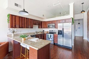 A modern kitchen with wooden cabinets, stainless steel appliances, and a granite countertop. - Cozy Broughton Street Retreat | Walk to Everything (Savannah)
