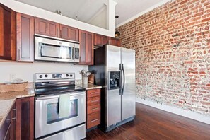 A kitchen with wooden cabinets, a stainless steel oven, a microwave, and a refrigerator. - Cozy Broughton Street Retreat | Walk to Everything (Savannah)