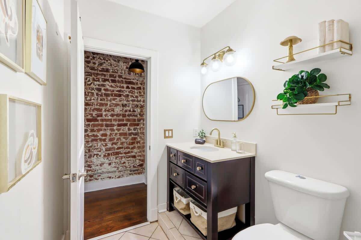 A bathroom with a white toilet, dark vanity, and a brick wall.