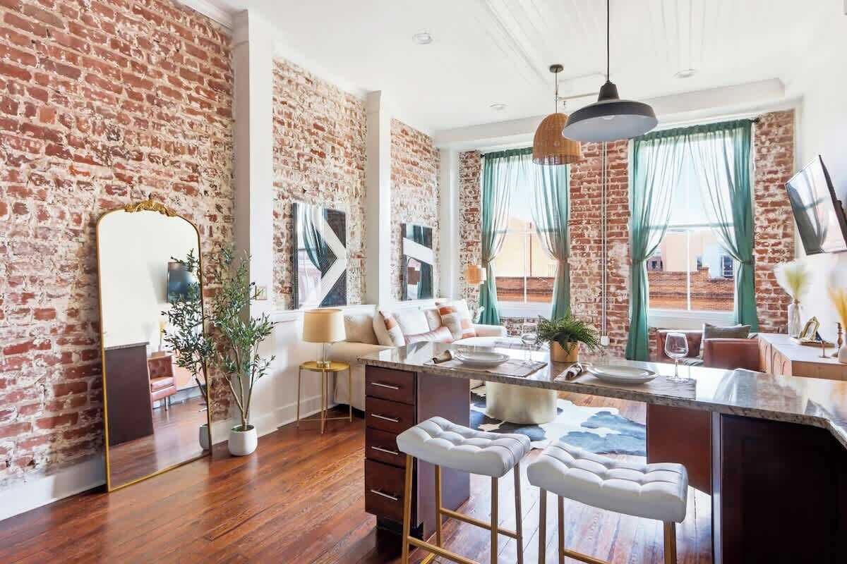A modern kitchen with a brick wall, a dining area with a sofa, and a bar with stools.