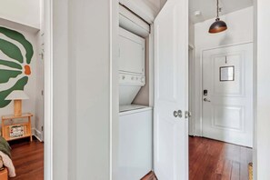 Une buanderie avec un lave-linge blanc, un plancher en bois et une porte ornée d’un cadre.