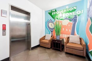 An elevator, two armchairs, a small table, and a wall with a colorful mural. - Cozy Broughton Street Retreat | Walk to Everything (Savannah)