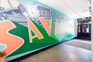 Un mur sur lequel le mot «SAVANNAH» est écrit en grandes lettres, une fresque représentant un paysage urbain et un panneau indiquant la sortie.