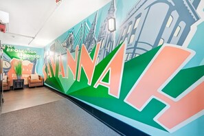 A hotel lobby with a large wall mural, seating area, and a sign for 'Broughton Condos'. - Cozy Broughton Street Retreat | Walk to Everything (Savannah)