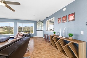 A spacious living area with a large window, a ceiling fan, and a wooden entertainment unit with decorative items. - Natures Escape - Game Room, Spa, Sauna, OMG Views! (Escondido)