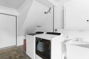 Ein Waschraum mit einer Frontlader-Waschmaschine und -Trockner, einem Waschbecken und einem Spiegel darüber.