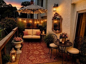 A cozy outdoor patio with a cushioned seating area, a table with chairs, string lights, and a decorative mirror. - The Magnolia Double En-Suite Townhome near Augusta National & Medical District (Augusta)