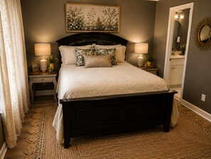 A bedroom with a dark wooden bed, two bedside lamps, a large framed artwork on the wall, and a woven rug on the floor. - The Magnolia Double En-Suite Townhome near Augusta National & Medical District (Augusta)