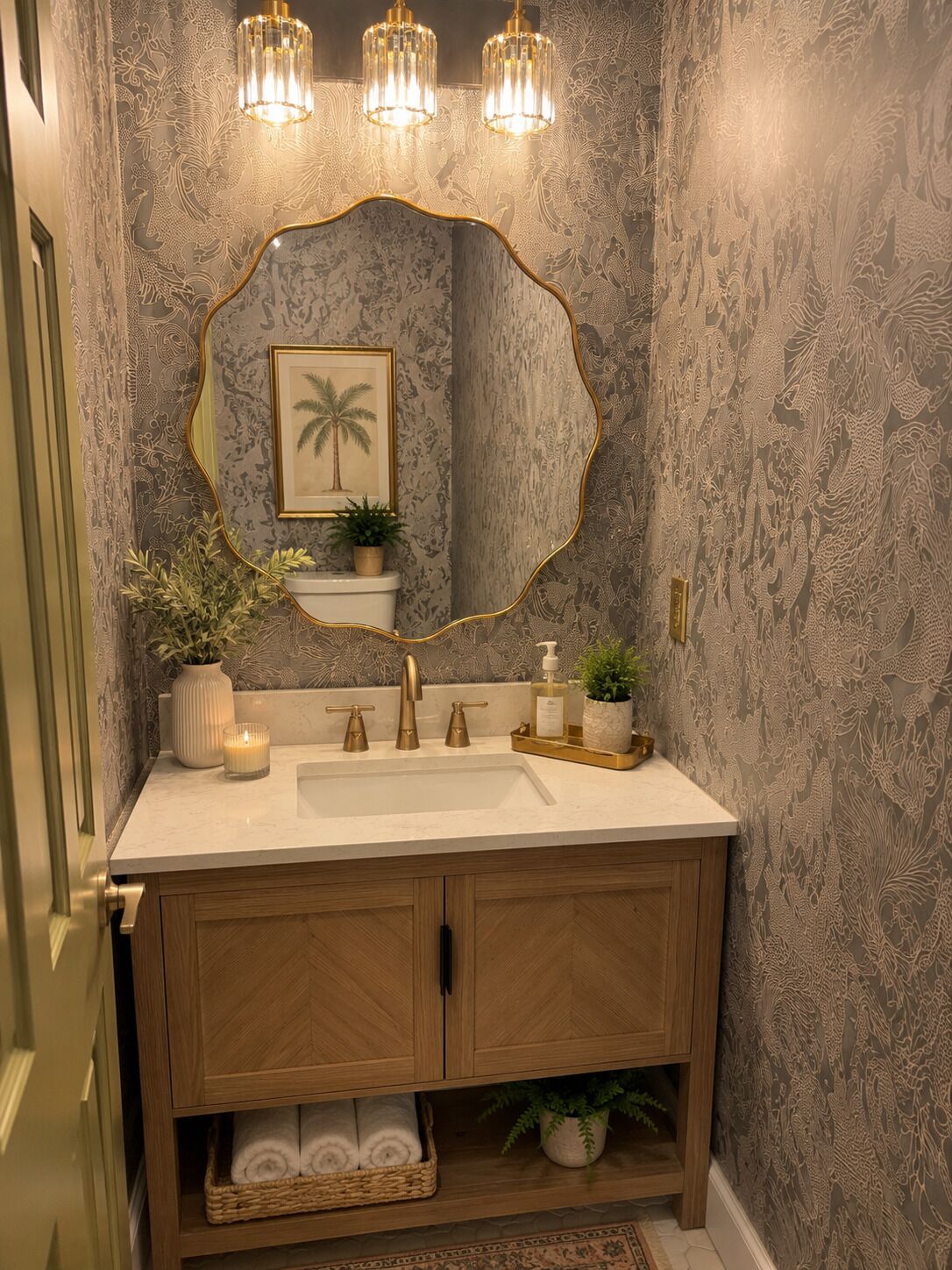 A bathroom with a vanity, a mirror with a gold frame, a towel rack, and a decorative plant.