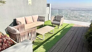 Ein moderner Außenbereich mit einer Sitzecke, inklusive Sofa, Stühlen und einem Tisch, mit Blick auf eine Stadtlandschaft.