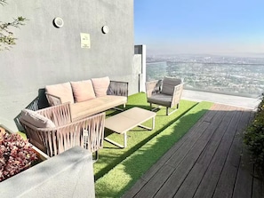 Ett modernt utomhusområde med sittmöbler, inklusive en soffa, stolar och ett bord, med utsikt över stadsbilden.