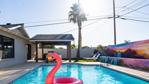 En pool med en uppblåsbar flamingofigur, en uteplats och en väggmålning.