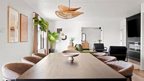 Ett modernt matområde med ett långt träbord, flätade stolar och en hängande lampa av flätat material.