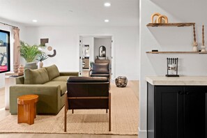A modern living room with a green sofa, a brown leather chair, and a small wooden stool. - Casa Sol - Desert Retreat w/ Pool & Large Patio 4 Bed/3bath (Scottsdale)