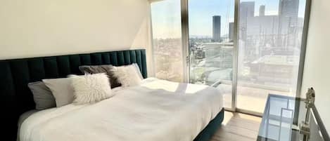 A modern bedroom with a large bed, a glass table, and a city view.