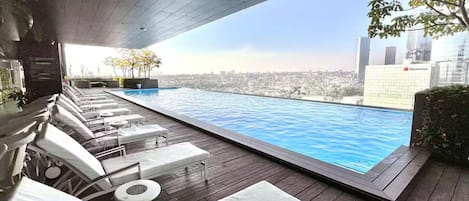 An infinity pool with lounge chairs and a city view.