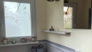 Ein Zimmer mit Fenster, das ein floralen Muster zeigt, einem Regal mit Dekoration, einem Spiegel und einer hölzernen Bank mit Schuhen.