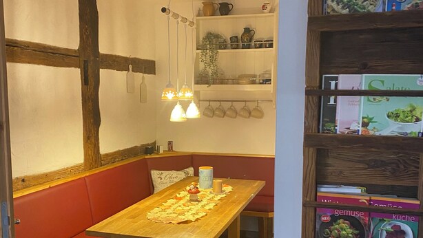 Ein Essbereich mit Holztisch, roter gepolsterter Bank, hängenden Pendelleuchten und einem Bücherregal mit Kochbüchern.