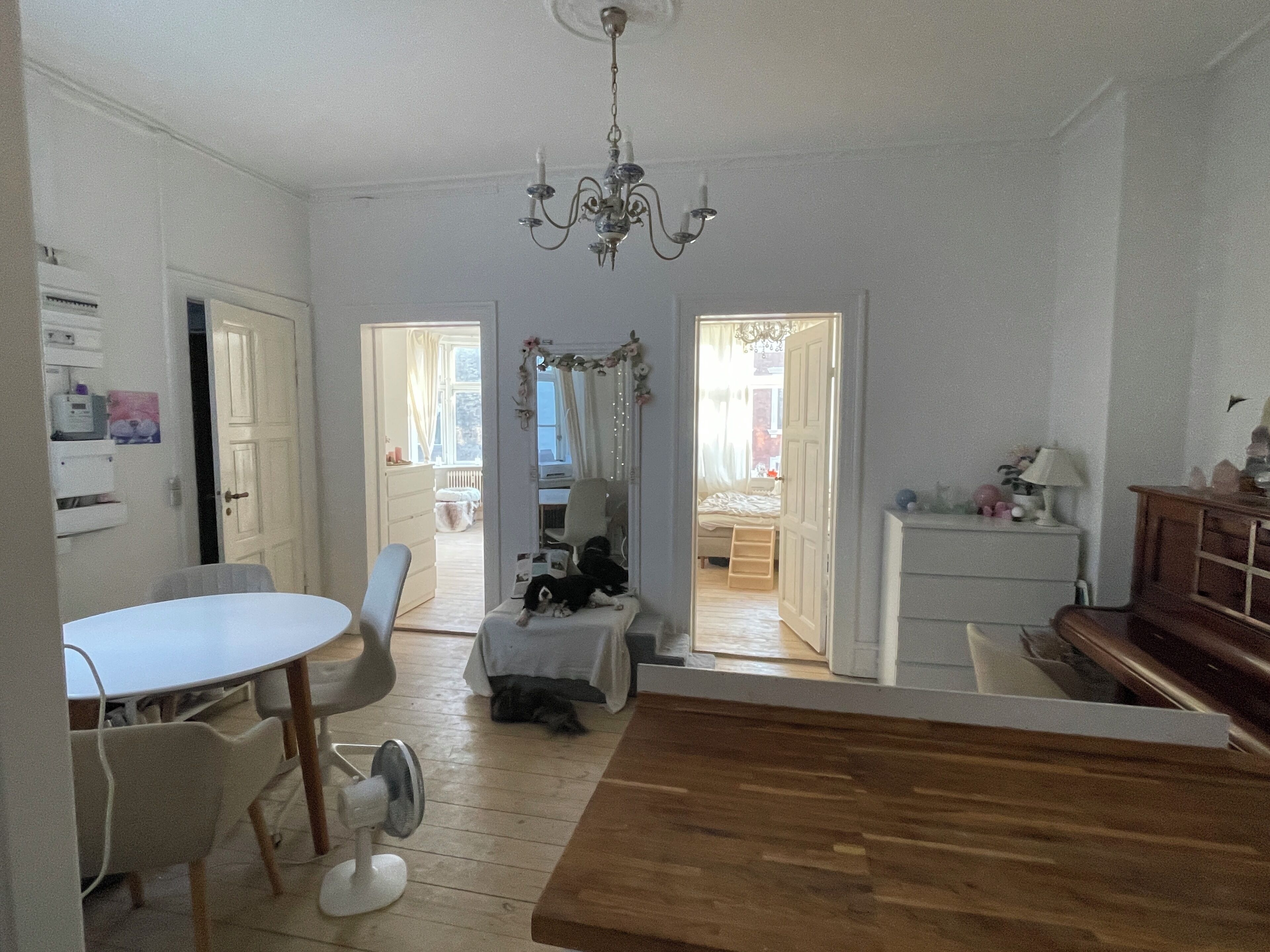 A room with a wooden dining table, chairs, a white cabinet, and a chandelier.