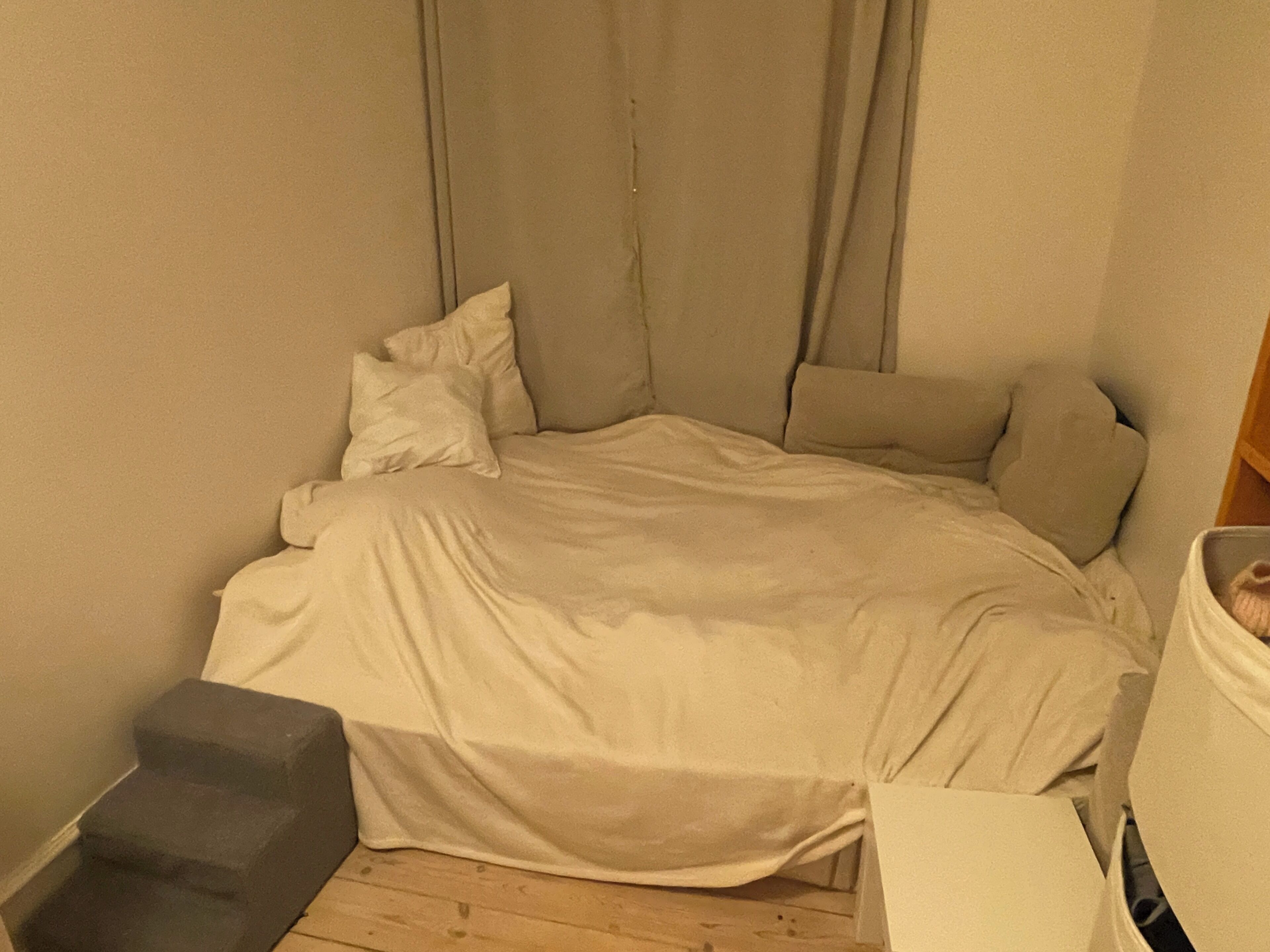 A small, single-bed room with a neutral color scheme, a bedside table, and a wardrobe.