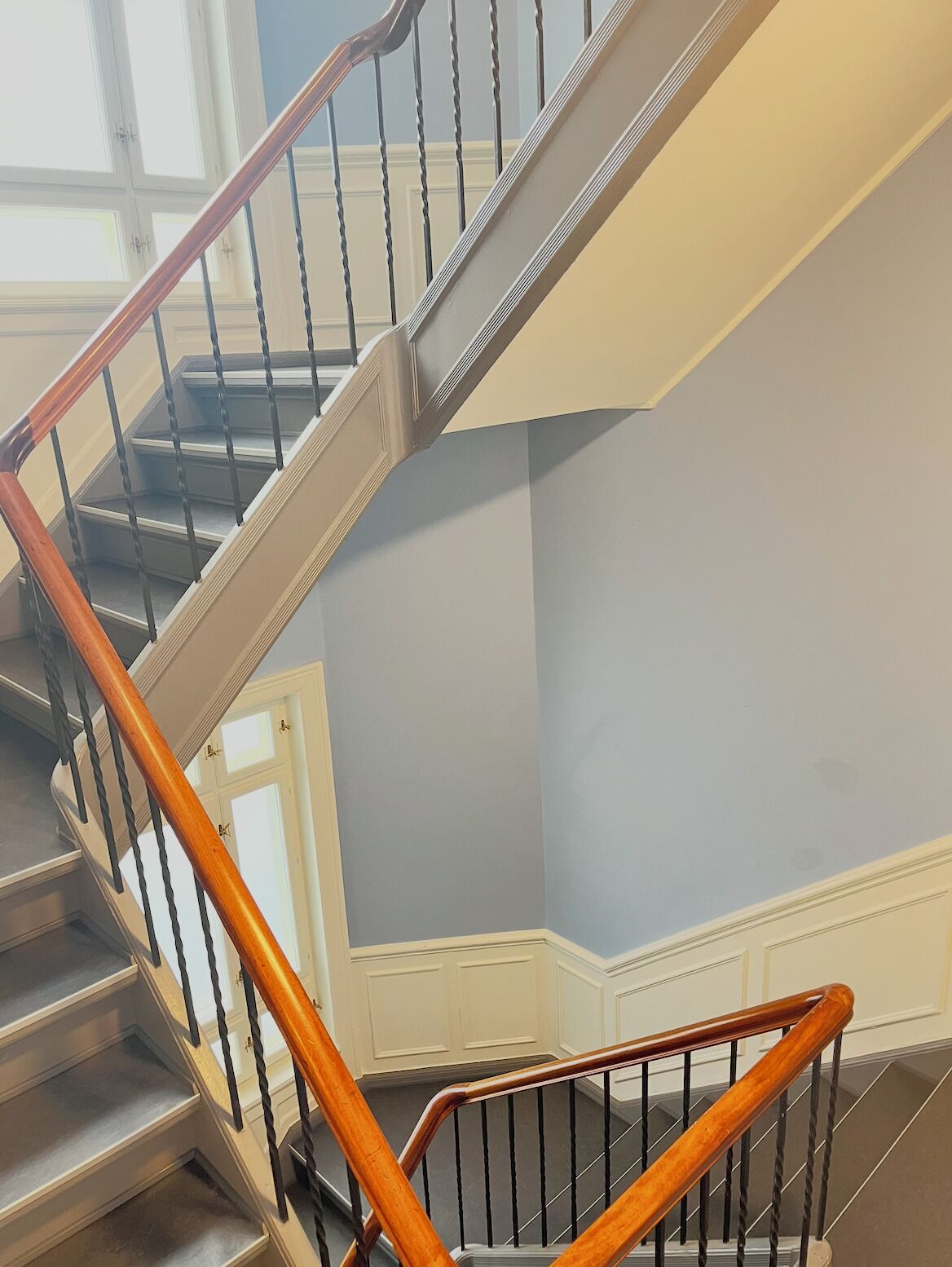 A spiral staircase with wooden handrails and metal balusters, leading to a landing with a white door.
