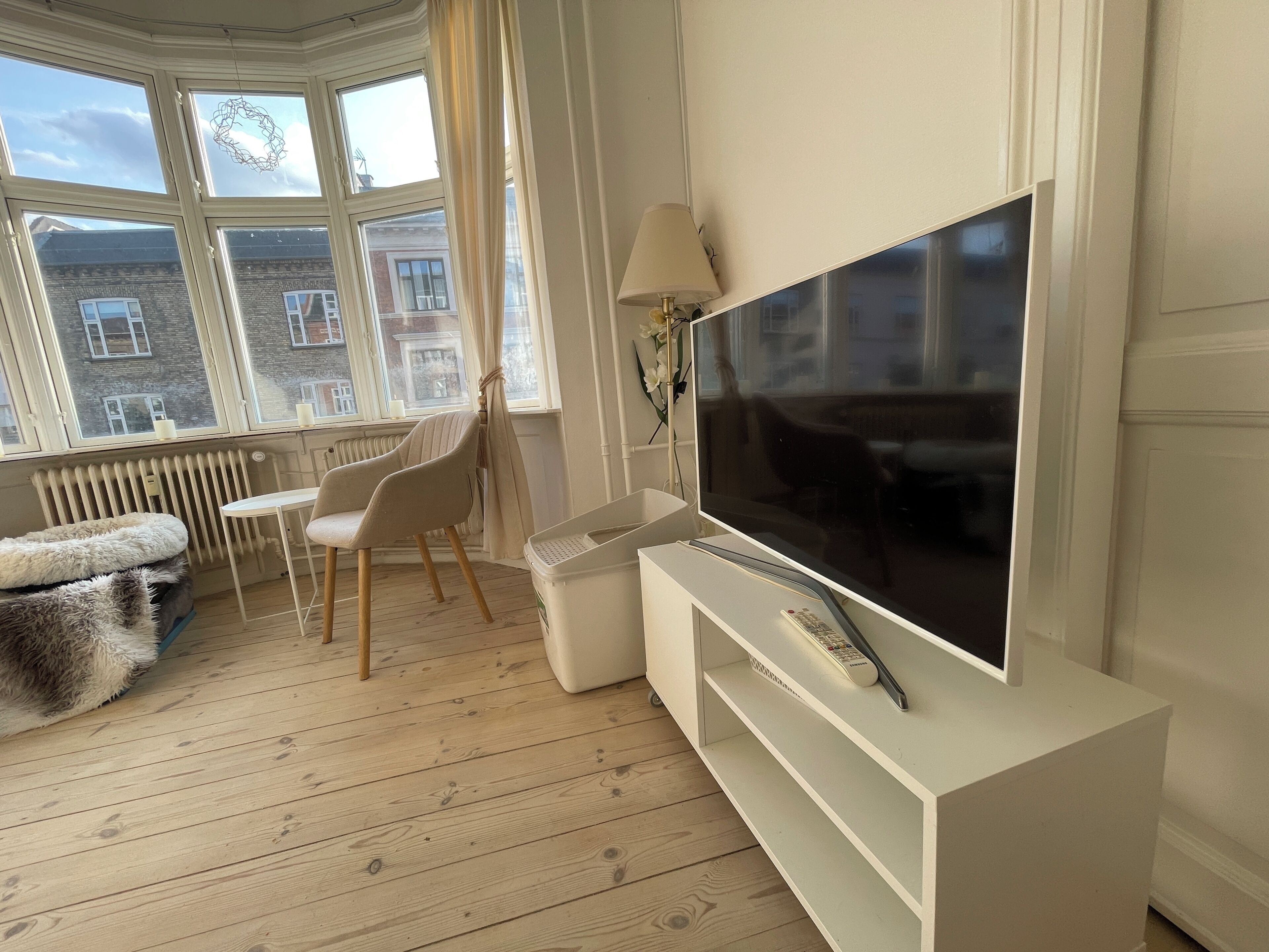 A modern living room with a large flat-screen TV, a white sofa, a small table, and a chair.