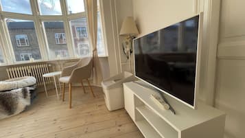 A modern living room with a large flat-screen TV, a white sofa, a small table, and a chair.