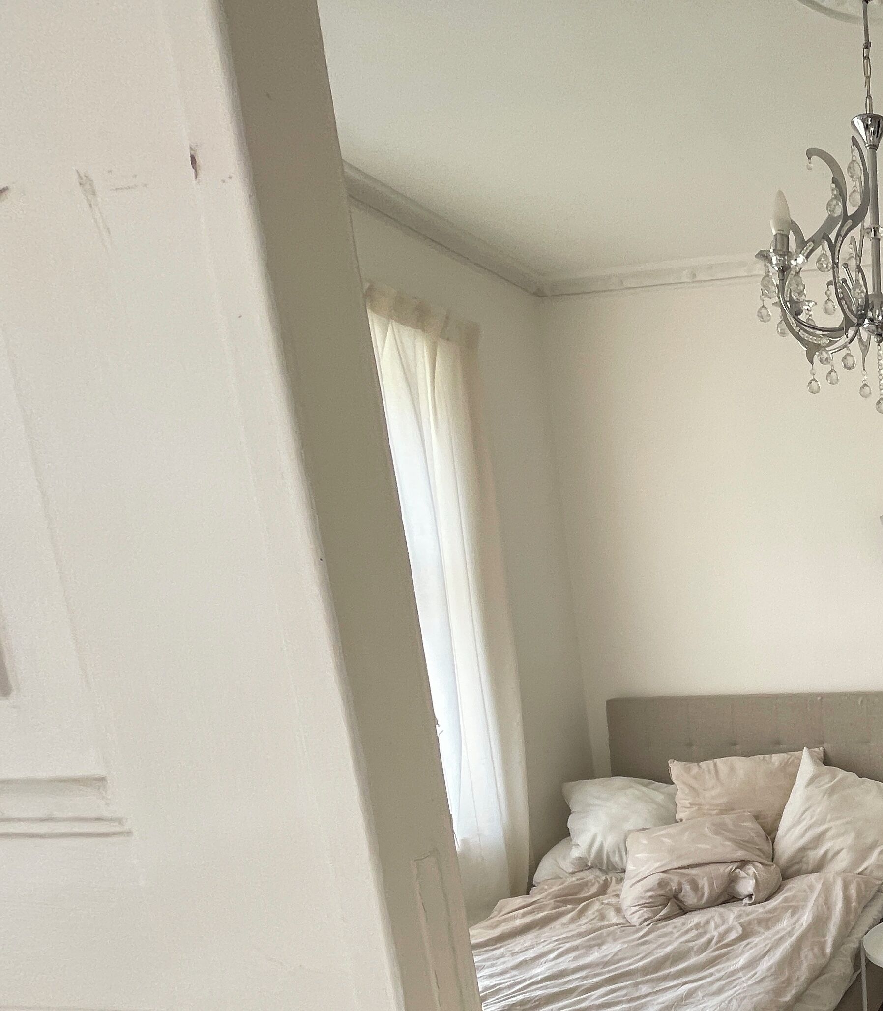 A bedroom with a bed, a chandelier, and a window with curtains.