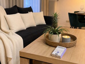 Ein gemütlicher Wohnbereich mit Sofa, Couchtisch, Topfpflanze, Kerze und einem Gesellschaftsspiel.