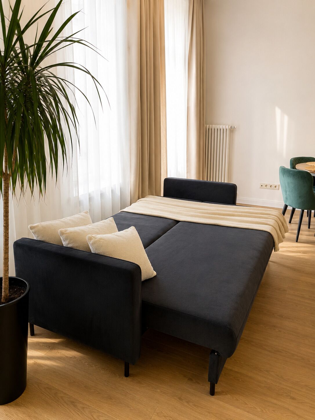A modern bedroom with a bed, a potted plant, and a dining area with chairs.