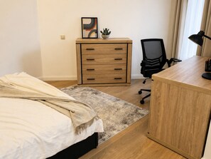 Ein Schlafzimmer mit einem Bett, einem Schreibtisch, einem Stuhl, einer Kommode und einer kleinen Pflanze.