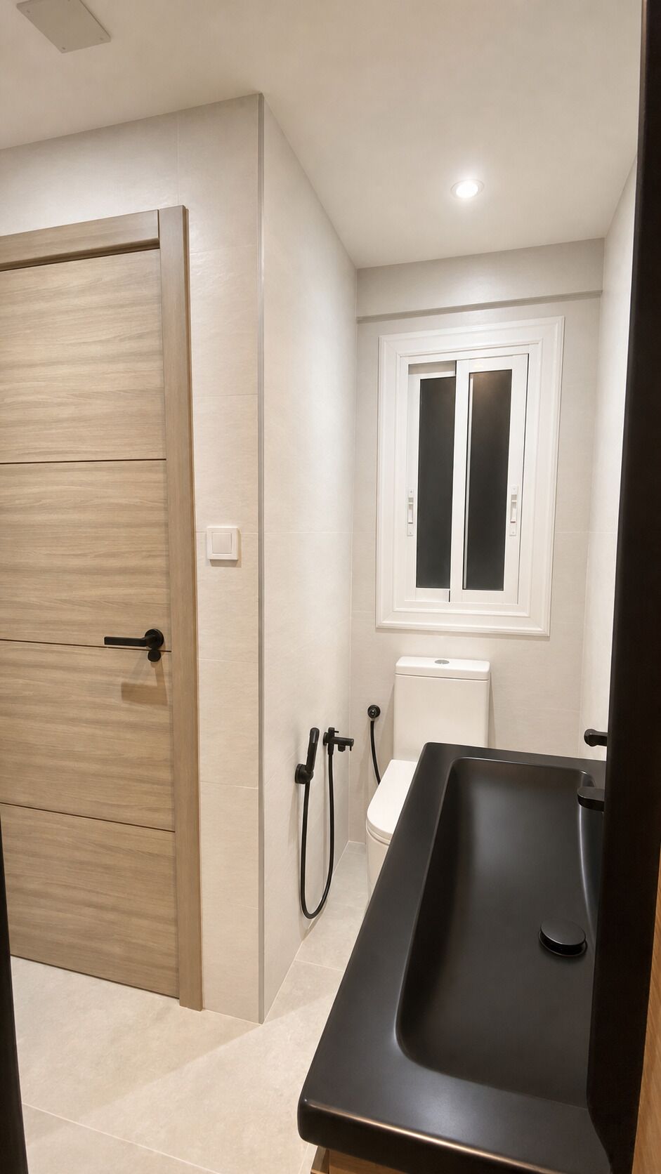 Et badeværelse med en trædør, et hvidt toilet, et sort badekar og et vindue over toilettet.