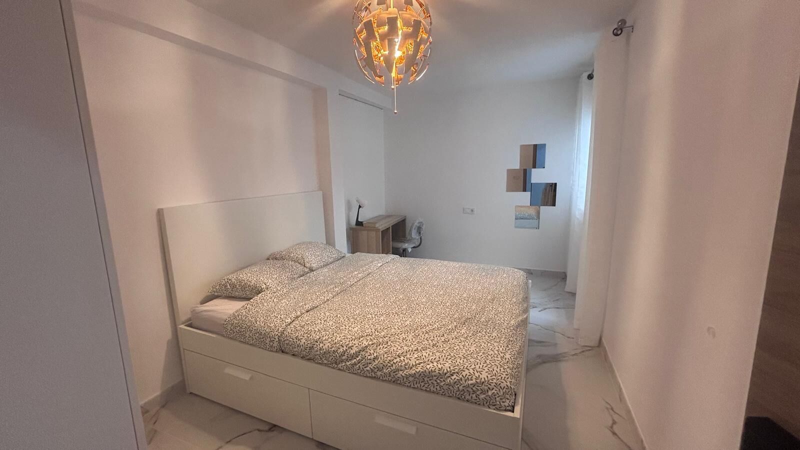 Une chambre à coucher comprenant un lit, une table de chevet, un miroir et un luminaire suspendu.