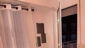 Un dormitorio con cama, cortina, puerta corrediza a un balcón y un estante pequeño fijado a la pared.