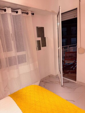 A bedroom with a bed, a curtain, a sliding door to a balcony, and a small wall-mounted shelf. - Central Apartment | Within Walking Distance of the Train Station and Downtown (alicante)