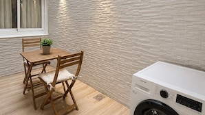 Un espacio práctico para la lavandería, con lavadora, mesa de madera y sillas, y ventana con persianas.