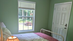 A bedroom with a bed, a bedside table with a lamp, a window, and a door. - Charming 4-bedroom modular home in Summersville, WV with private creek access. (Summersville)