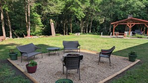 A patio area with outdoor furniture, a fire pit, and a gazebo in a wooded setting. - Charming 4-bedroom modular home in Summersville, WV with private creek access. (Summersville)
