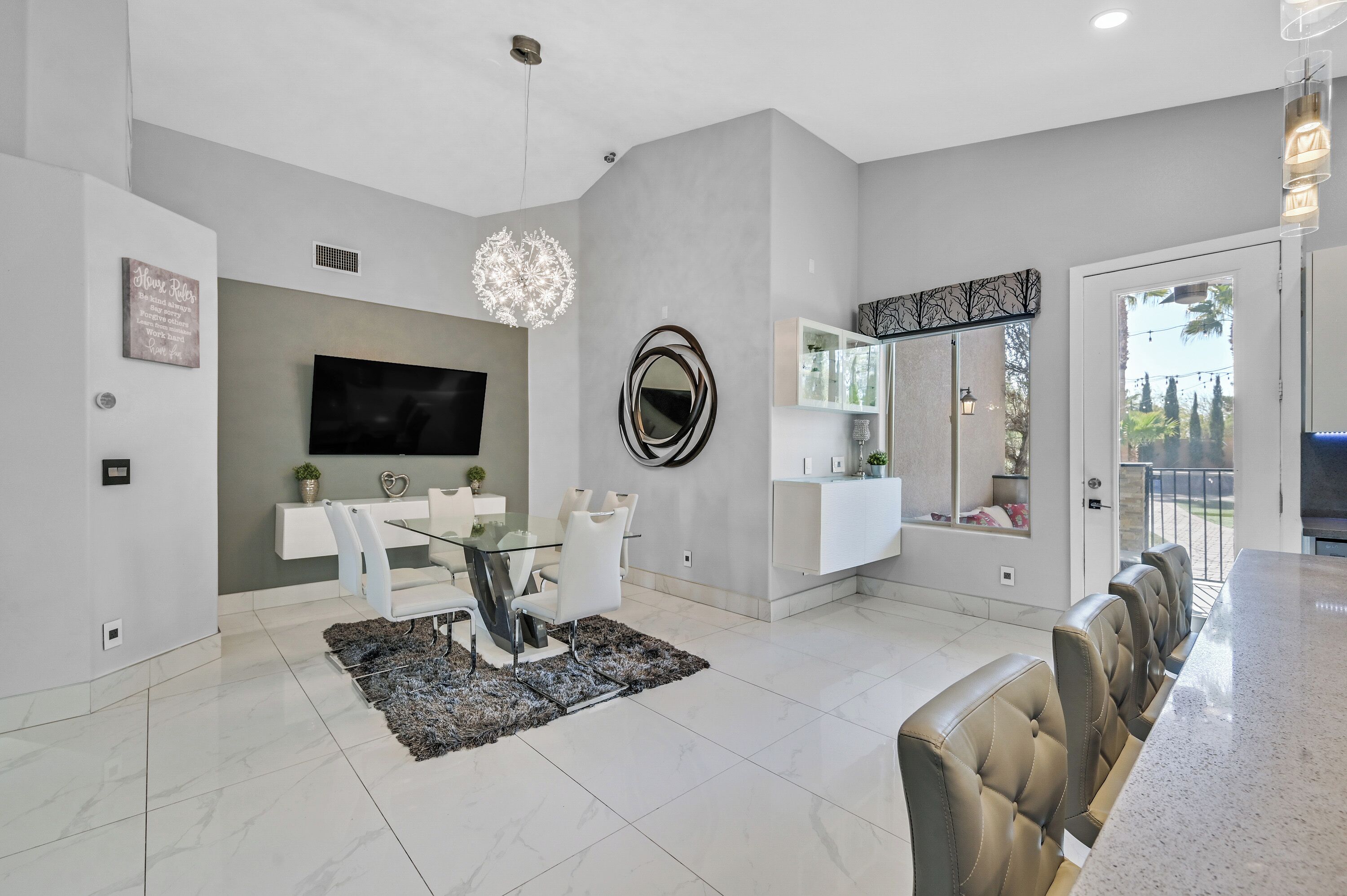 A modern dining area with a glass table, white chairs, a black rug, and a large mirror.
