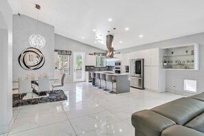 Eine moderne Küche mit Edelstahlgeräten, ein Essbereich mit Glastisch und ein Wohnzimmer mit Ledersofa.