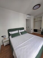 Una cama bien hecha con ropa de cama blanca y verde, una mesita de noche con lámpara y un armario con estantes.