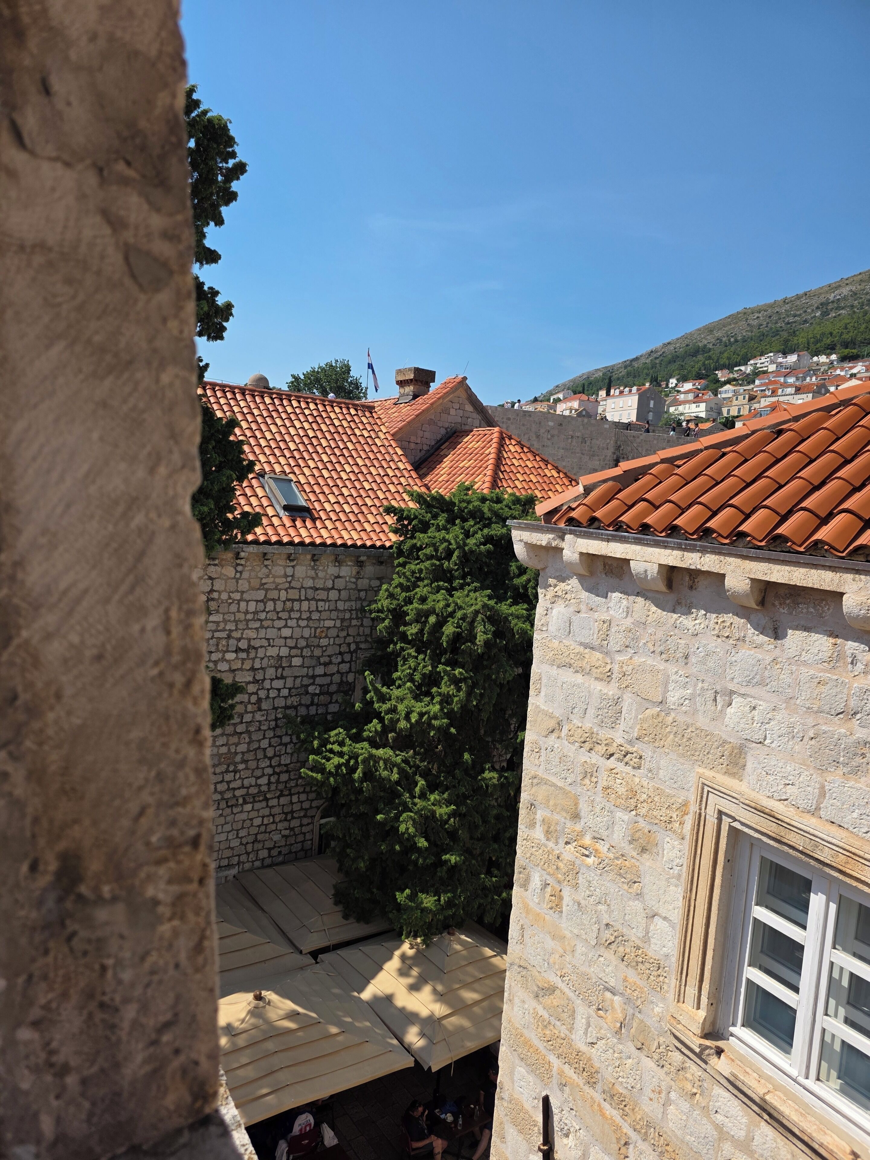 A courtyard with stone walls, a tiled roof, and a window with a view of a hillside.