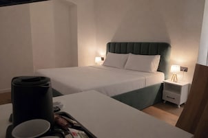 A hotel room with a bed, bedside tables, a coffee maker, and a tray with snacks.