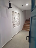 A hallway with a textured wall, a light fixture, a power outlet, and a wooden staircase.